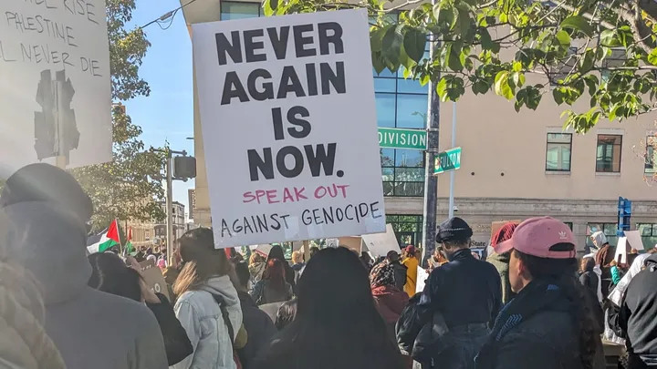 Protester holding sign that reads, "Never again is now. Speak out against genocide."